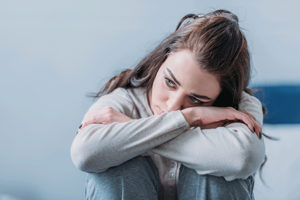 A woman sitting with her head on her knees is experiencing the effects of trauma.