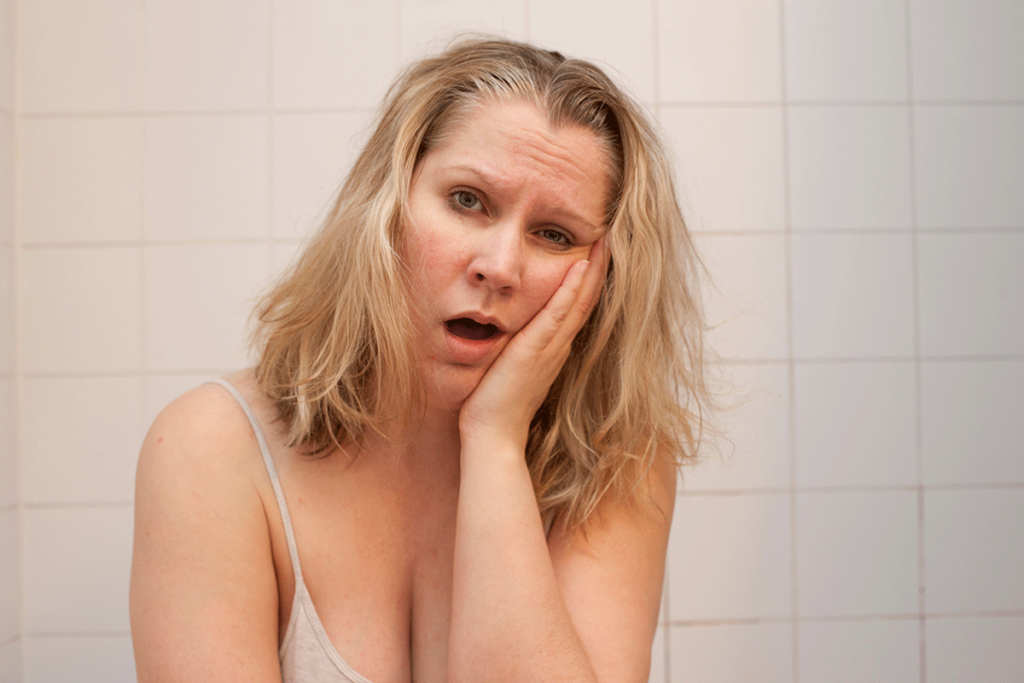 A woman sits with her palm to her face, she is experiencing the long-term effects of meth abuse.