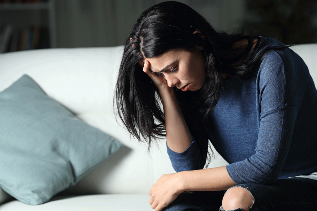 A woman is experiencing the impact of trauma and addiction. She is sitting with her head in her hands.