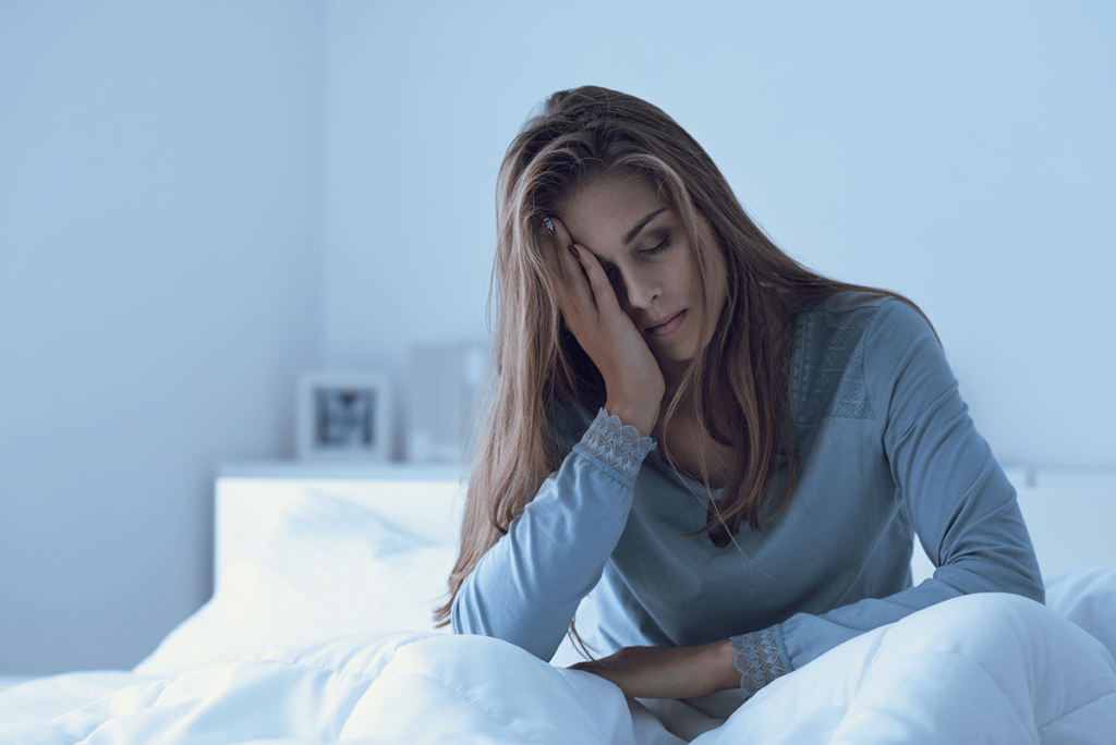 A woman is sitting in bed and holding her head in her hands. She is experiencing Valium side effects.